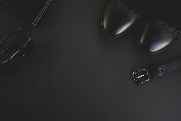 Fashion man accessories on black background. Shoes, leather belt, wallet and sunglasses. Top view, flat lay, copy space