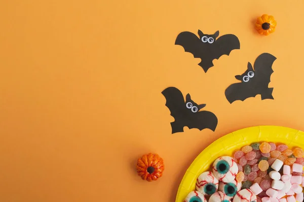 万圣节的概念 万圣节装饰 黑纸蝙蝠 橙色背景的糖果 复制空间 平躺在地上 俯瞰四周 — 图库照片