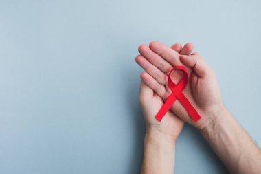 Erkek elleri açık mavi arka planda kırmızı kurdele farkındalığı tutar. Tıp konsepti, Dünya Cinsel Sağlık Günü. Üst görünüm, alanı kopyala