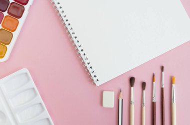 Not defteri, suluboya ve pastel pembe arka planda fırçalar. Sanat malzemeleri. Üst görünüm, düz görünüm, kopyalama alanı