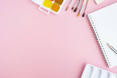 Resim malzemeleri ve pastel pembe arka planda not defteri. Üst görünüm, düz görünüm, kopyalama alanı