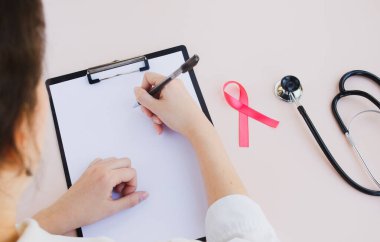 Göğüs kanseri ve tıbbi konsept. Doktor boş bir panoya yazı yazıyor. Göğüs kanserinin pembe kurdele sembolü ve arka planda steteskop. Üst görünüm