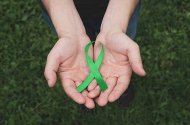 Yeşil Akıl Sağlığı Farkındalığı kurdelesi insanın ellerinde. Tıp ve sağlık hizmetleri kavramı. Kapat, üst görünüm