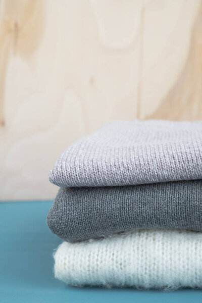 Stack of knitted sweaters on blue wooden table. Warm clothes. Close up, vertical, copy space