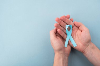 Açık mavi prostat kanseri farkındalığı kurdelesini açık arka planda tutuyor. Tıp ve sağlık konsepti, erkek sağlığı. Boşluğu kopyala, üst görünüm