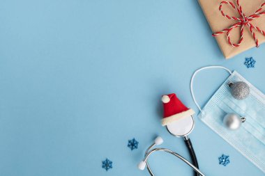 Kırmızı Noel Baba şapkalı tıbbi steteskop hediye kutusu, yüz koruma maskesi ve arka planda şenlik dekorasyonu. Noel ve Yeni Yıl kartpostalları. Yeni normal, koronavirüs salgını konsepti