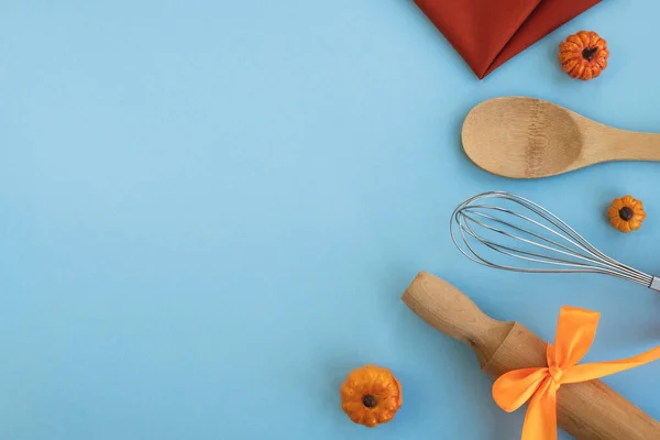 Halloween or Thanksgiving day cooking background. Rolling pin, whisk, wooden spoon, linen napkin and decorative pumpkins on light blue table. Top view, flat lay, copy space