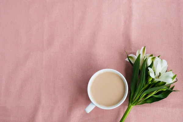 Cup of coffee with flowers on pastel pink tablecloth. Morning composition, greeting card. Top view, flat lay, copy space
