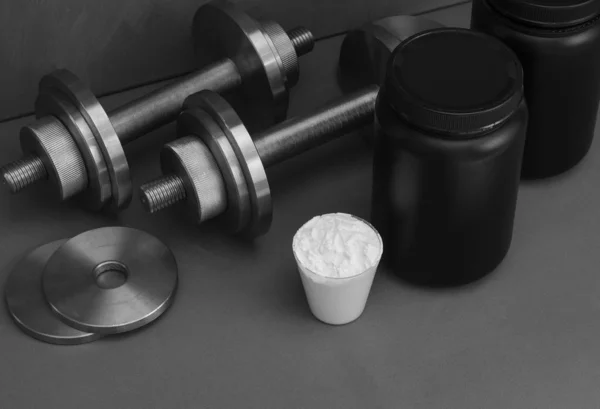 Sports nutrition with dumbbells on a gray background.