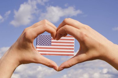 Aşk jesti - Amerikan bayrağının arka planında mavi gökyüzünün arka planında duran kalp. Amerikan tatili.