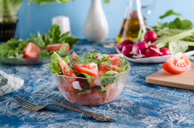 Sebzeli salata ve mavi arka planda şeffaf bir salata kasesinde otlar. Sağlıklı beslenme