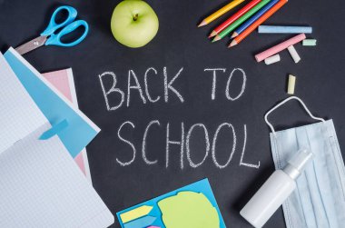 Okuldaki siyah arkaplan, okul malzemeleri, yüz kalkanı ve antiseptikler. Koronavirüs salgını sırasında eğitim.