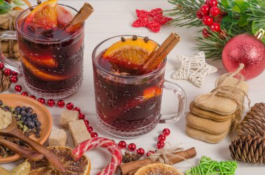 Portakal dilimli sıcak şarap, elma, tarçın çubuğu ve beyaz ahşap arka planda baharatlar..