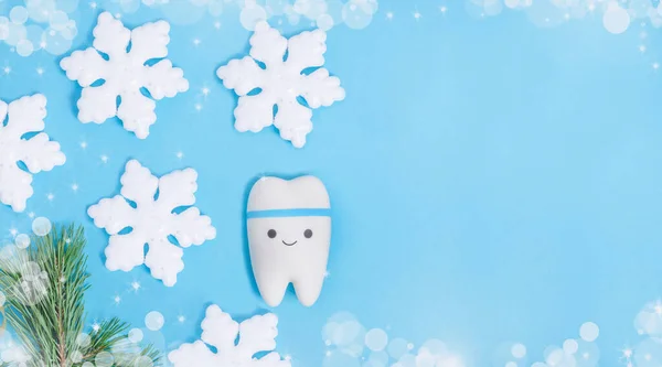 Baner for dentistry for Christmas and New Year with a tooth model on a blue background with a Christmas decor from snowflakes with copy space.