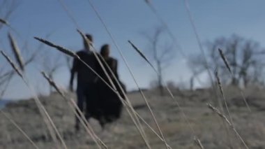 Arka planda bir elbise genç adam ve kadın rüzgar bir fırıncılık açık gökyüzü kulakları tarafından üfleme ön planda odaklı doğaya el tutarak yürüyor.
