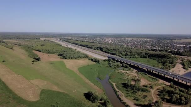 Panorama d'en haut avec vue sur le village de maisons privées, un pont sur lequel passent les voitures, forêt, rivière, clairière. Une journée d'été claire et ensoleillée, un ciel sans nuage.Le drone réduit la hauteur .