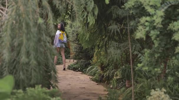 반바지와 흰색 재킷을 입은 슬림 한 소녀가 식물원, 열대 지방에서 걷습니다. — 비디오