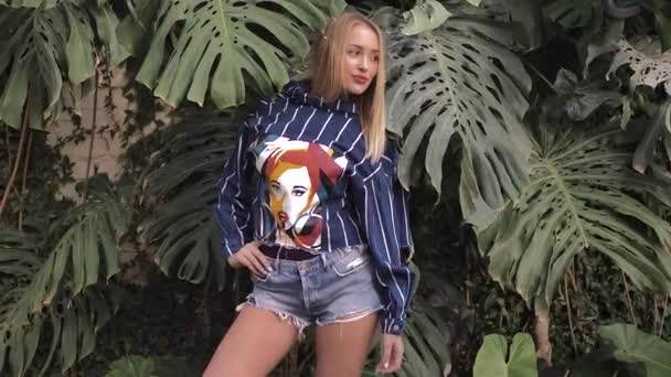 Beautiful blonde posing in front of the camera. Tropical plants in background — Stock Video