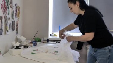 siyah bir t-shirt ve kot pencerenin yanındaki ceket tüyleri üzerinde çalışıyor esmer. Beyaz duvarda bir sürü çizim var..