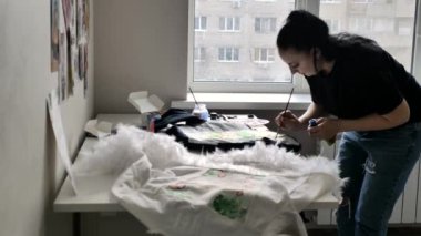 siyah bir t-shirt ve kot bir esmer ceket pencereye yakın bir boğa terrier bir illüstrasyon çizer. Beyaz duvarda bir sürü çizim var..