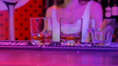 Kız barmen bara bardağı koydu ve ortadan kayboldu. Arka planda - alkol şişeleri ile bir vitrin. Oda mor ışıklarla aydınlatılmış..