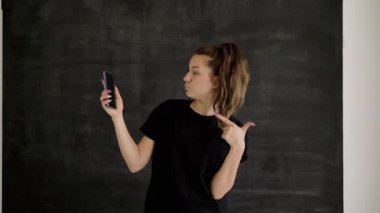 Spor giyim Kafkas esmer elinde bir akıllı telefon tutar, diğer eliyle duygusal gadget ekranında ilginç ve komik bir şey gösterir, arka plan siyah