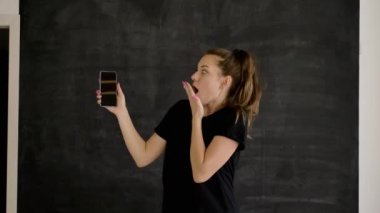 Spor giyim Kafkas esmer elinde bir akıllı telefon tutar, diğer eliyle duygusal gadget ekranında ilginç ve komik bir şey gösterir, arka plan siyah