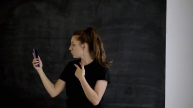 Spor giyim Kafkas esmer elinde bir akıllı telefon tutar, diğer eliyle duygusal gadget ekranında ilginç ve komik bir şey gösterir, arka plan siyah