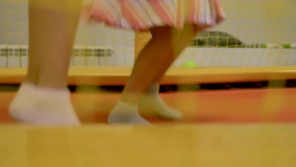 两个小女孩跳上黄色的蹦床 在白色袜子的特写腿 在背景 — 图库视频影像