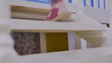Pembe sandaletli çocuk ayakları beyaz oyuncak merdiveninde aşağı yukarı koşar, yakın çekim.