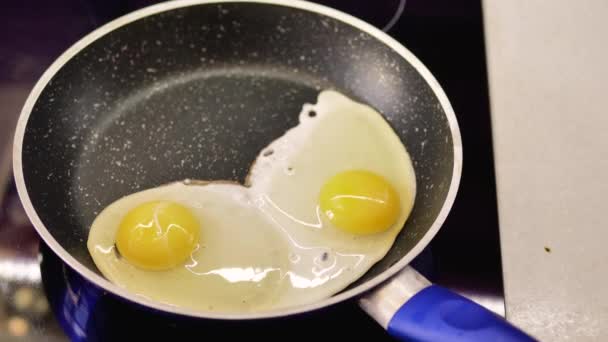 青いハンドルを持つフライパンで揚げた2つの鶏の卵 トップビュー — ストック動画