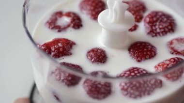 Blender altından şeffaf bir fincan, kırmızı çilek yüzen beyaz süt, yakın çekim.