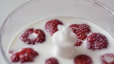 Blender altından şeffaf bir fincan, kırmızı çilek yüzen beyaz süt, yakın çekim.