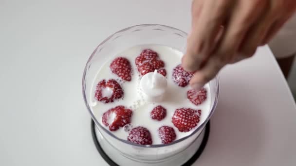 特写镜头 女性双手将草莓放入牛奶中 放在一个透明的搅拌杯中 搅拌机站在白色桌子上 顶视图 — 图库视频影像