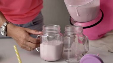Kadın elleri şeffaf bir cam kadeh içine pembe milkshake dökün, yanında pembe elbise ve kot pantolon bir kız.