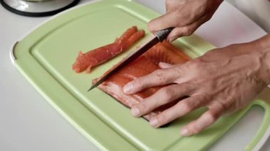 Kadın elleri bıçakla kesilmiş açık yeşil kesme tahtasıüzerinde bir parça somon, doğal ışık, yakın çekim.