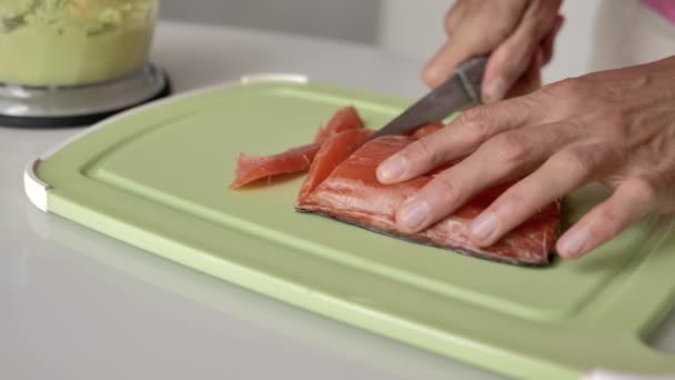 女性双手用刀在浅绿色的切板上切一片鲑鱼 自然光线 — 图库视频影像