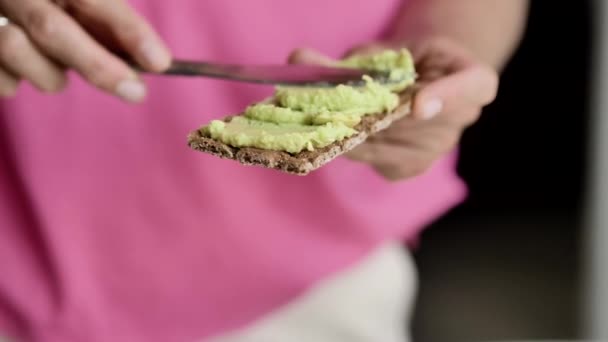 女性の手はトーストにナイフで緑色のペーストを塗りつぶし 表面に均等に分配し クローズアップ 自然光 — ストック動画