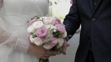 Gelin ve damat el ele tutuşuyor. Aralarında bir düğün buketi var. Yakın plan..