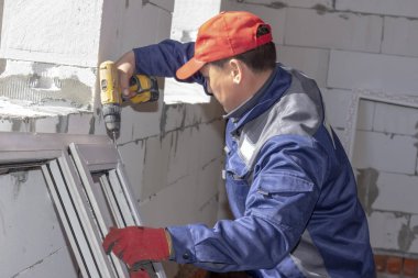 İşçiler inşaat halindeki bir eve cam döşüyorlar, ölçümler, matkaplar, testere öğütücüleri yapıyorlar.