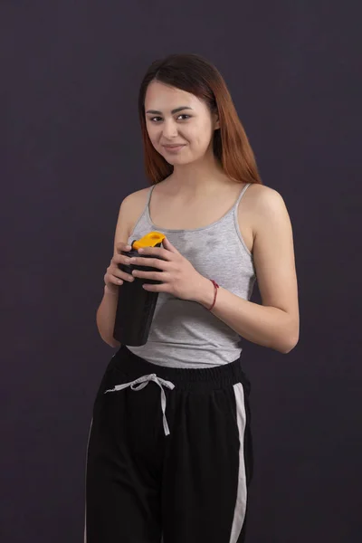 sports girl after playing sports drinks from a shaker with a wet shirt from sweat on a dark background