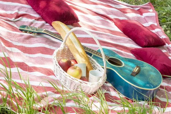 summer picnic basket with apples and guitar lie on a plaid with pillows heat