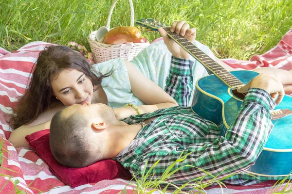 the guy plays the guitar to his girlfriend. romantic meeting. summer picnic couple laying on the grass