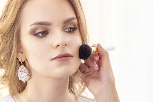makeup artist applies beautiful model powder and blush with a big brush on face