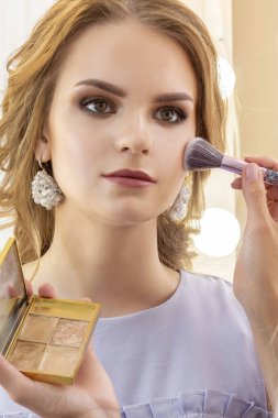 Makyaj sanatçısı kız modeli makyaj koyar. Elmacık kemikleri ve yüzünde fırça tozu. güzel kız modeli, portre. Makyajçıplak renkler. düğün, akşam makyajı. dikey fotoğraf