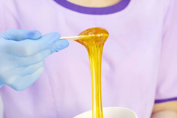 Liquid sugar for skin epilation. Close up shot. depilation and beauty concept - sugar paste or wax honey for hair removing with wooden waxing spatula sticks