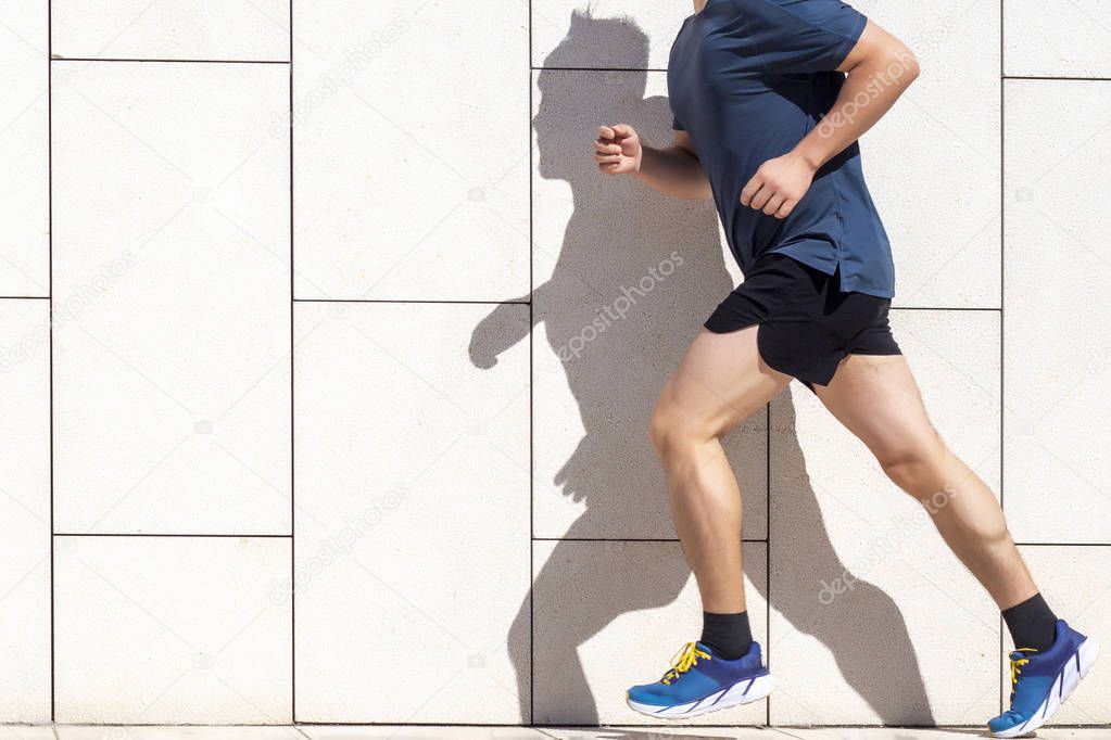 A man jogging on a track with his shadow on the wall. Handsome man running in the city. Fitness, workout, sport, lifestyle concept