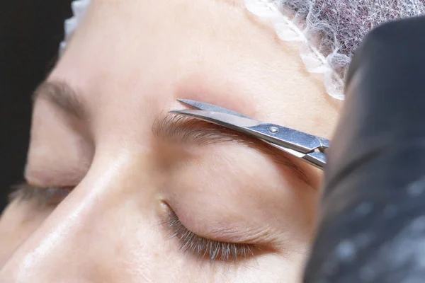 eyebrow shaping in a beauty salon. the girl is trimmed with scissors for extra hair on her eyebrows. master brows