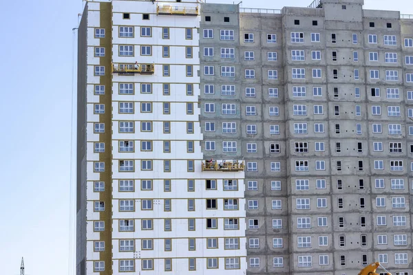 Facade work and insulation of a multistory building. Professional construction workers on the scaffold elevator insulated wall facade with mineral wool. roofers wearing safety harness insulating wall facade at height on old building in a crane