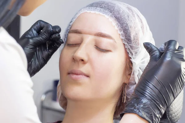 eyebrow dyeing. beauty saloon. the girl lies with her eyes closed on the eyebrow dyeing procedure. preparation of eyebrows for painting. applying cream around the eyebrows using thread.